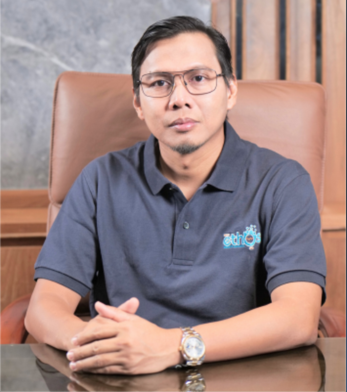 Professional headshot of Indonesian male executive in smart business attire, warm smile, office background